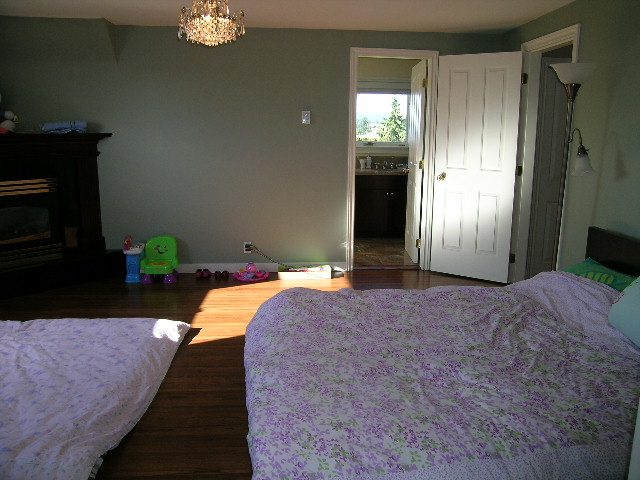 Spacious bedroom with hardwood floors, floral bedspread, and a cozy fireplace. - 1875 26th Street, West Vancouver