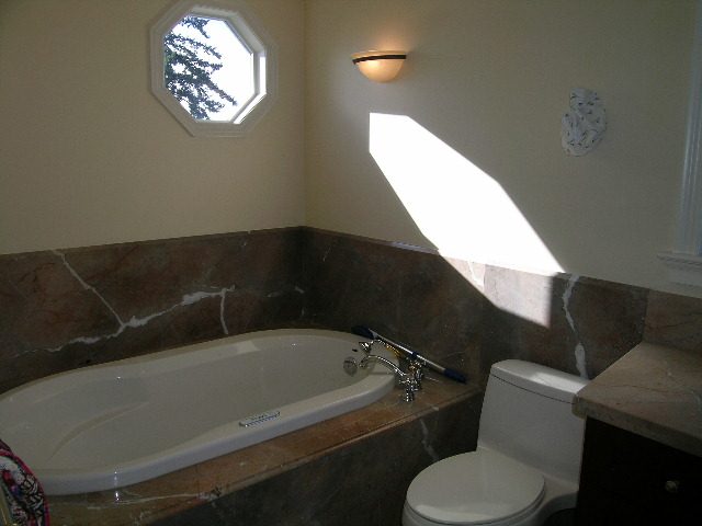Spacious bathroom with a marble countertop and a large octagonal window. - 1875 26th Street, West Vancouver