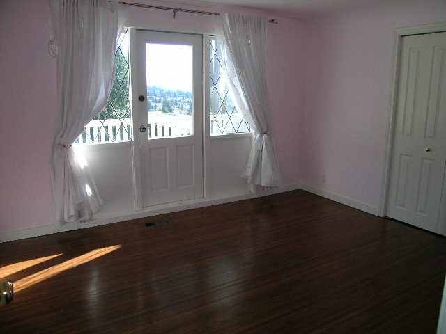 Spacious living room with hardwood floors, white curtains, and a view of the city through the French doors. - 1875 26th Street, West Vancouver