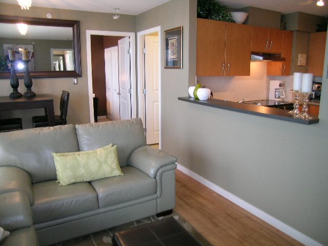 Spacious living room with leather couch, hardwood floors, and kitchen counter in the background. - 2109 - 1295 Richards Street, Vancouver Downtown