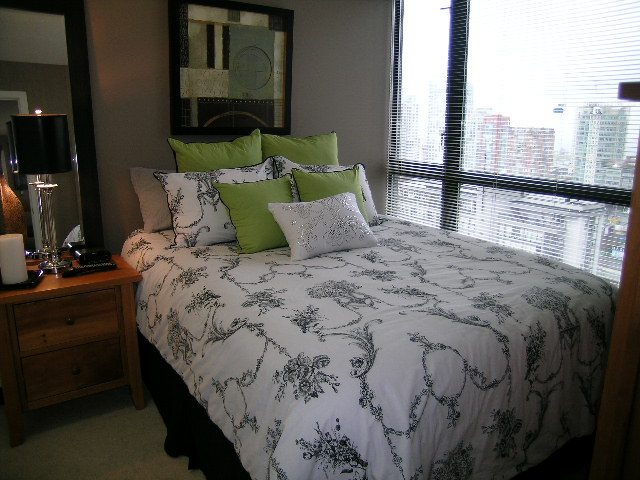 Spacious bedroom with a city view, featuring a comfortable bed with green and white bedding and a wooden nightstand.