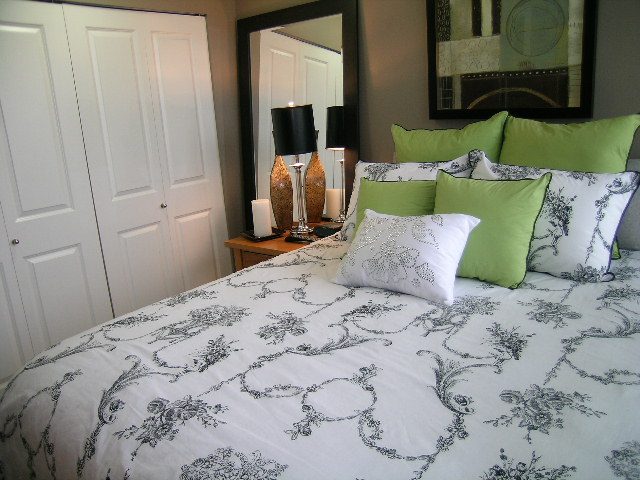 Spacious bedroom with elegant toile bedding, green accent pillows, and a large mirror reflecting the cozy ambiance.