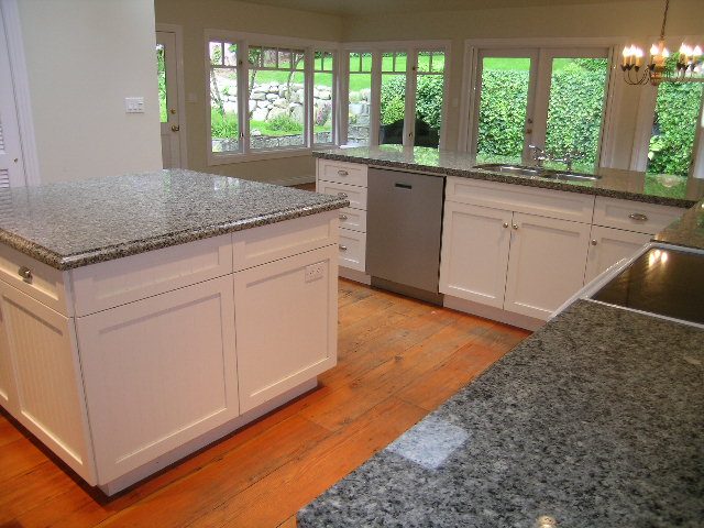 Bright kitchen with granite countertops, white cabinets, and hardwood floors, showcasing a serene garden view.