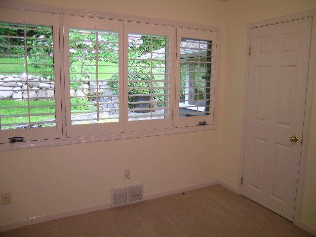 Spacious living room with large bay window and white shutters, leading to a serene garden view. - 2795 Palmerston Avenue, West Vancouver