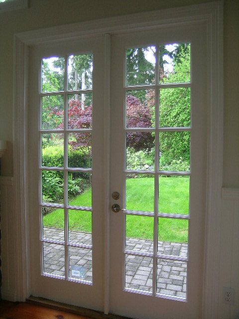 Spacious living room with French doors leading to a garden, showcasing lush greenery and brick patio. - 2795 Palmerston Avenue, West Vancouver