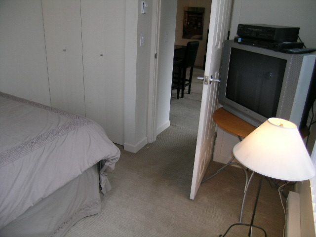 Bright bedroom with neatly made bed, closet, and small TV. - 302-977 Mainland Street, Vancouver Downtown