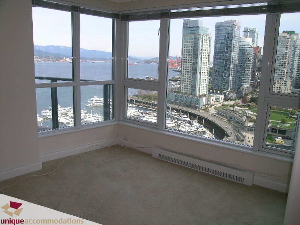 Spacious living room with panoramic city and water views, featuring large windows and a neutral carpet. - 1903 - 535 Nicola Street, Vancouver Downtown