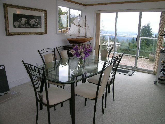 Bright dining room with glass table, white chairs, and a city view through large windows. - 1104 Hillside Road, West Vancouver
