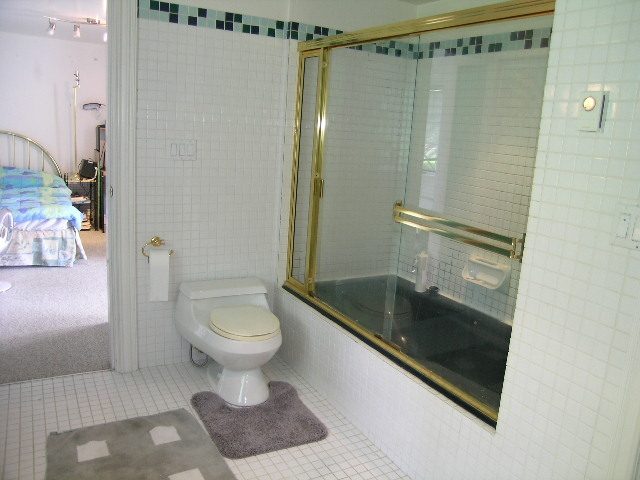 Furnished bathroom with gold-framed glass shower, white tile, and gray bath mat. - 1104 Hillside Road, West Vancouver