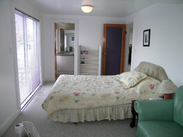Furnished bedroom with floral bedding, large window, and cozy seating area. - 1104 Hillside Road, West Vancouver