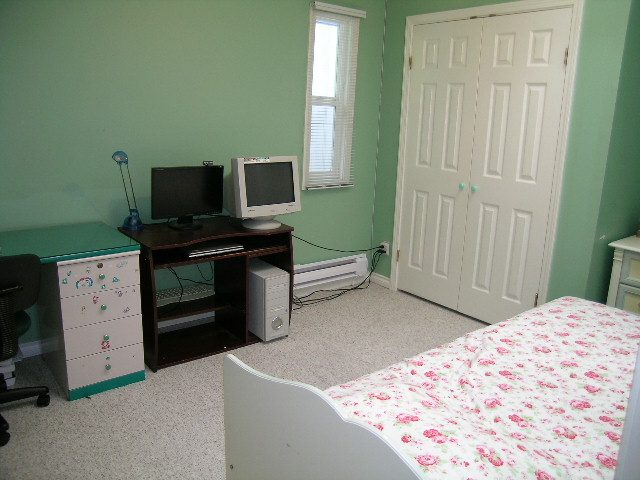 Bedroom with floral bedding and a desk setup, light green walls, white closet doors. - 983 Canyon Boulevard, North Vancouver