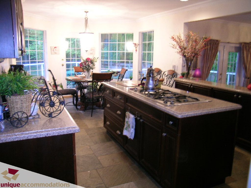 Bright kitchen with granite countertops, dark cabinetry, and a dining area in the background. - 5735 Nancy Green way, North Vancouver