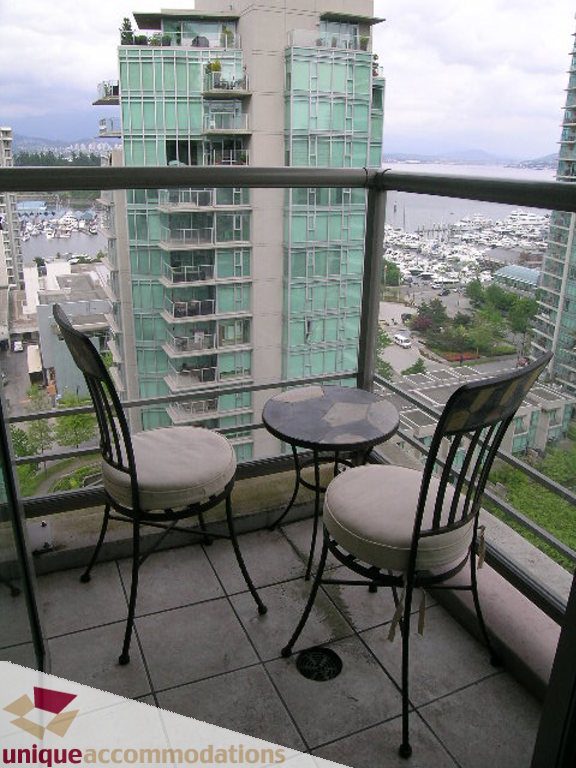 Balcony with a city view, furnished with a small table and two chairs, overlooking marinas and greenery.