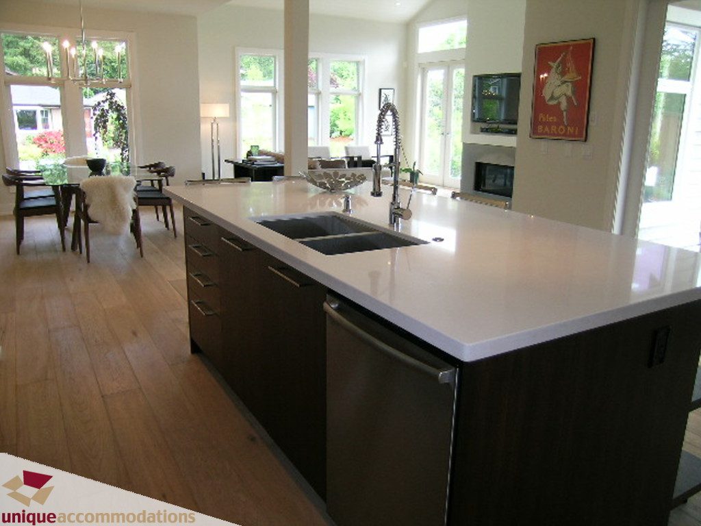 Modern kitchen with white countertops, dark cabinets, and hardwood floors, featuring a central island and large windows.