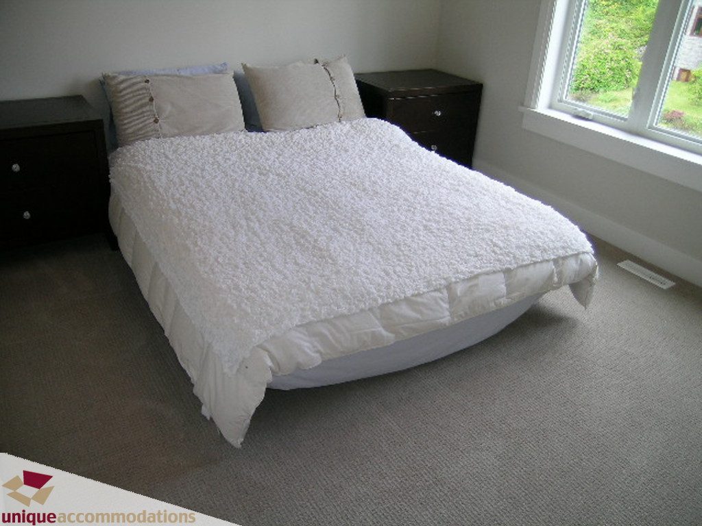 Spacious bedroom with white bedding, large window, and dark nightstands. - 2015 Lloyd Avenue, North Vancouver