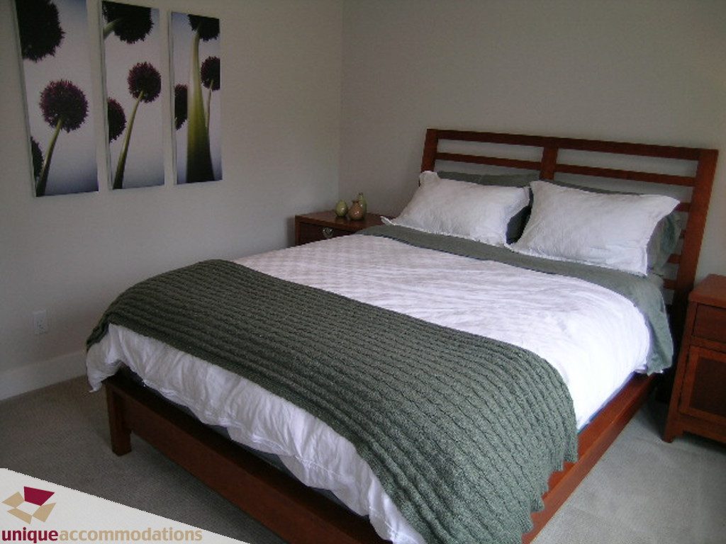 Spacious bedroom with wooden headboard, green throw blanket, and modern art on the wall. - 2015 Lloyd Avenue, North Vancouver