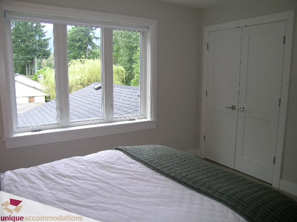 Spacious bedroom with large windows offering a serene view of trees and rooftops. - 2015 Lloyd Avenue, North Vancouver