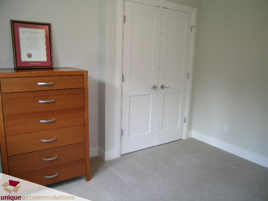 Spacious bedroom with wooden dresser and double closet doors, neutral carpet and light walls. - 2015 Lloyd Avenue, North Vancouver
