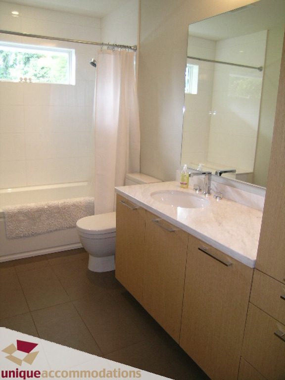 Modern bathroom with light wood cabinets, white marble countertop, and a large mirror. - 2015 Lloyd Avenue, North Vancouver