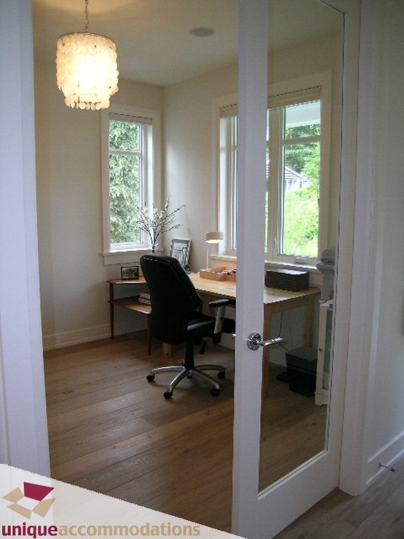 Spacious home office with hardwood floors, large windows, and a comfortable desk setup. - 2015 Lloyd Avenue, North Vancouver