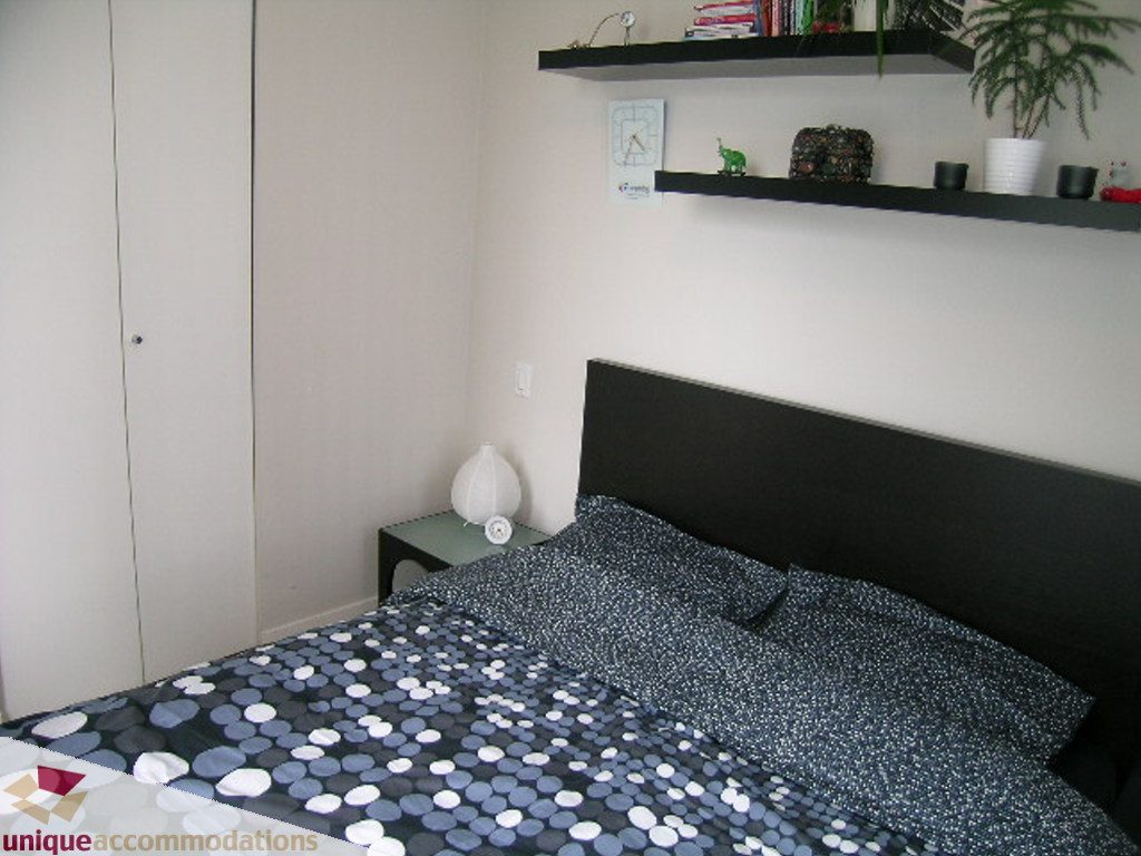 Furnished bedroom with black headboard, patterned bedding, and floating shelves. - 707 - 1010 Richards Street, Vancouver Downtown