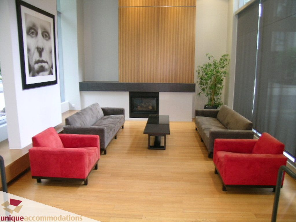Furnished living room with red armchairs, hardwood floors, and a large portrait on the wall. - 707 - 1010 Richards Street, Vancouver Downtown