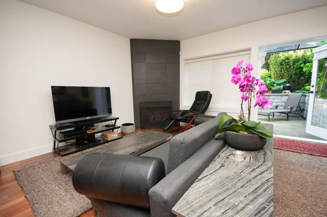 Living room with gray sofa and marble-top coffee table, featuring pink orchids and modern fireplace. - 2447 West 6th Ave., Vancouver West Side