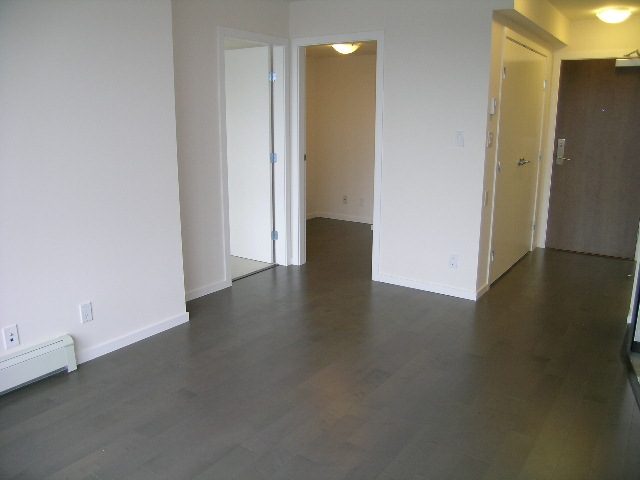 Open-concept living space with hardwood floors and a door leading to a private den. - 808 - 1887 Crowe St, Vancouver West Side