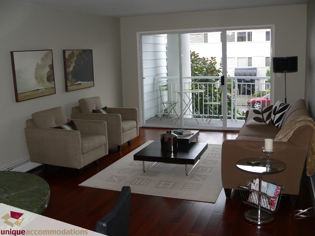Furnished living room with hardwood floors, modern furniture, and a city view through sliding glass doors.