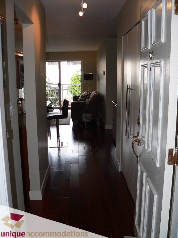 Furnished hallway leading to living area with hardwood floors and city view. - 203 - 1066 W 13th Ave, Vancouver West Side