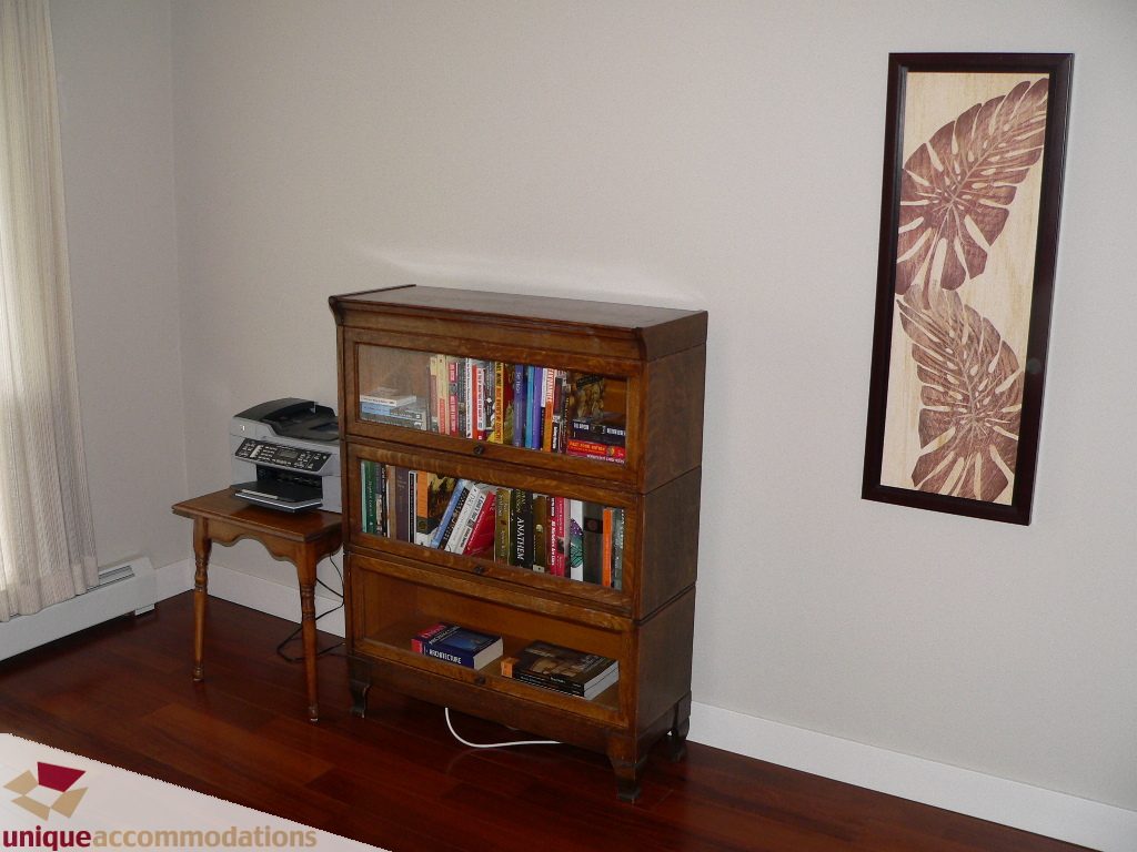Bright living room with hardwood floors, a bookshelf, and a framed leaf artwork. - 203 - 1066 W 13th Ave, Vancouver West Side