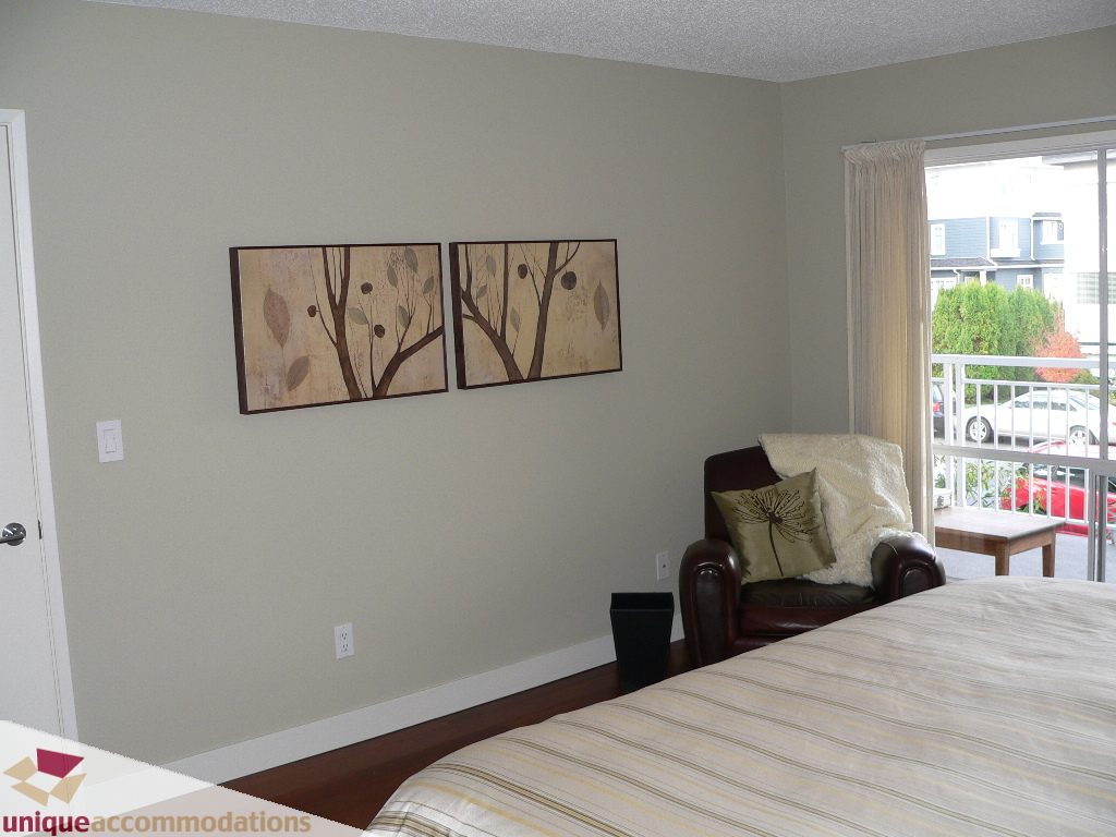 Furnished bedroom with striped bedding, wall art, and balcony view. - 203 - 1066 W 13th Ave, Vancouver West Side