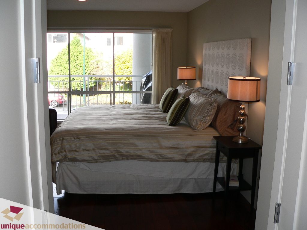 Furnished bedroom with hardwood floors and a balcony view. - 203 - 1066 W 13th Ave, Vancouver West Side