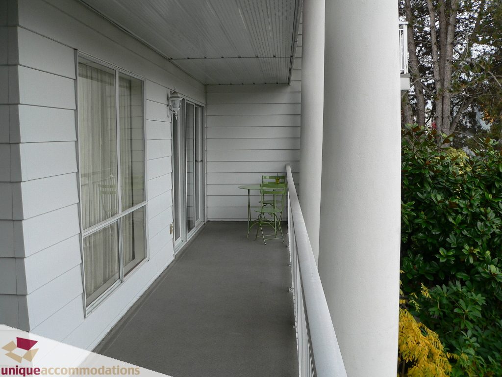 Furnished balcony with white walls, green plants, and a view of trees. - 203 - 1066 W 13th Ave, Vancouver West Side