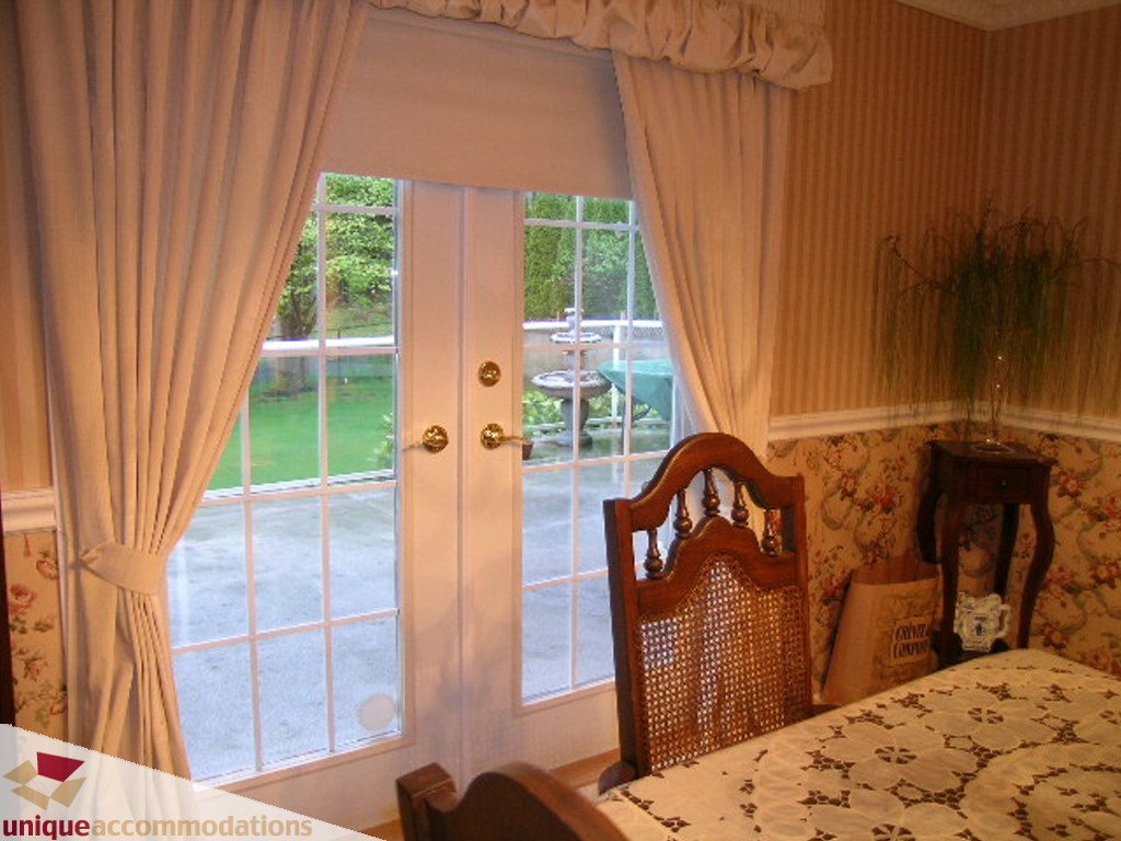 Bright bedroom with large windows, floral bedspread, and lush greenery outside. - 5735 Nancy Green way, North Vancouver