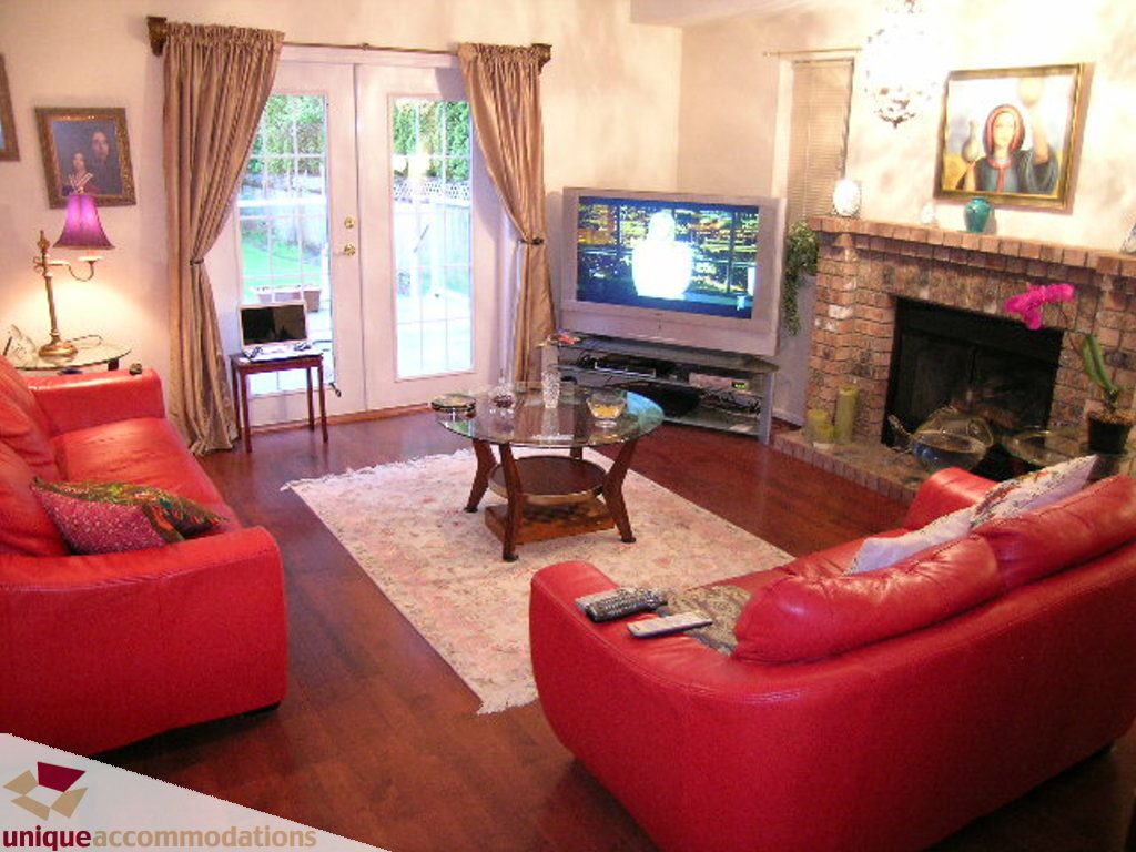 Furnished living room with red leather couches, hardwood floors, and a fireplace. - 5735 Nancy Green way, North Vancouver