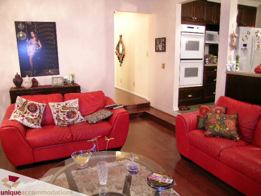 Bright living room with red leather couch, glass coffee table, and kitchen in the background. - 5735 Nancy Green way, North Vancouver