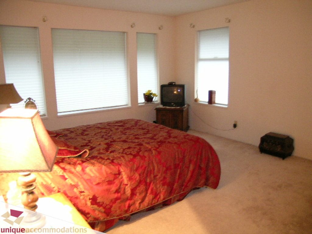 Furnished bedroom with red patterned bedding and multiple windows. - 5735 Nancy Green way, North Vancouver