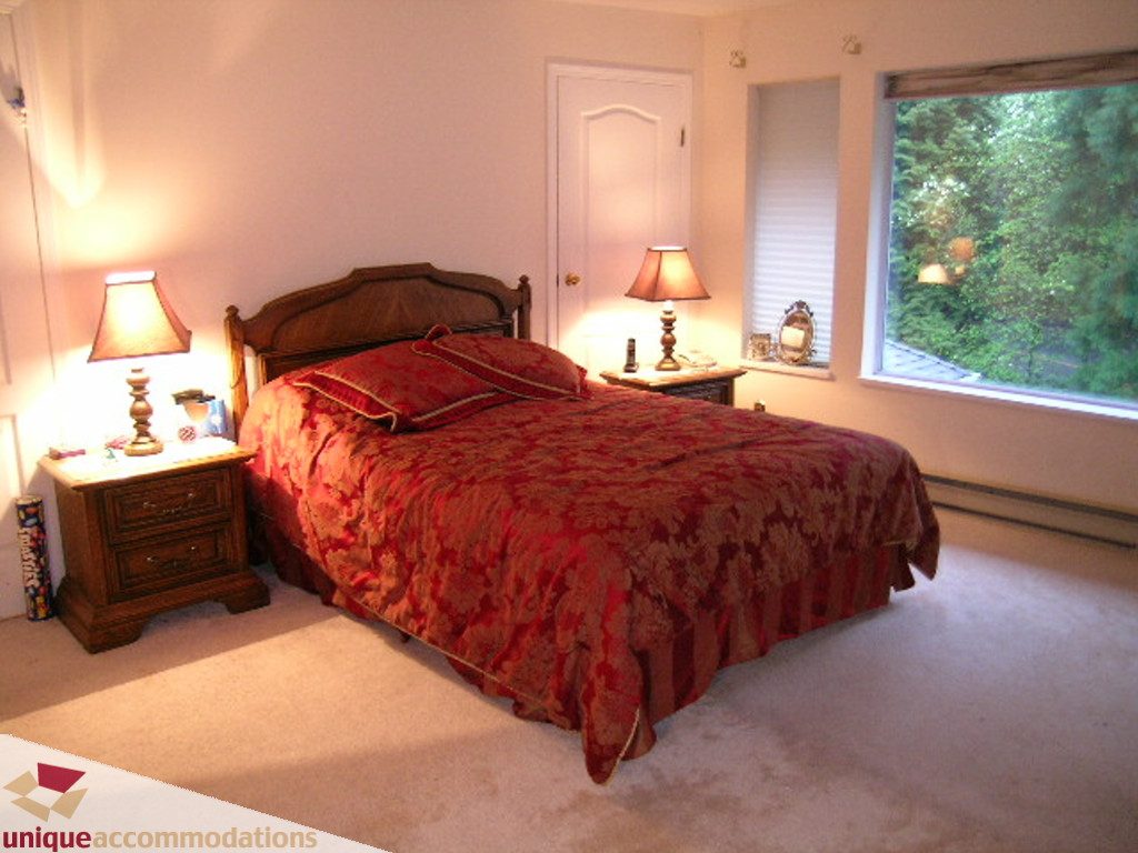 Spacious bedroom with red patterned bedding and large window view. - 5735 Nancy Green way, North Vancouver