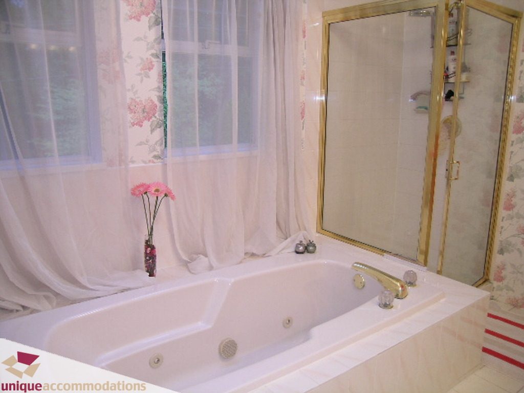 Bathroom with large soaking tub, floral curtains, and gold-framed mirror. - 5735 Nancy Green way, North Vancouver