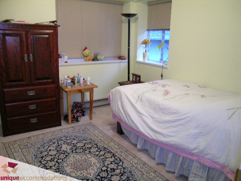 Bright bedroom with wooden furniture, floral bedspread, and patterned rug. - 5735 Nancy Green way, North Vancouver