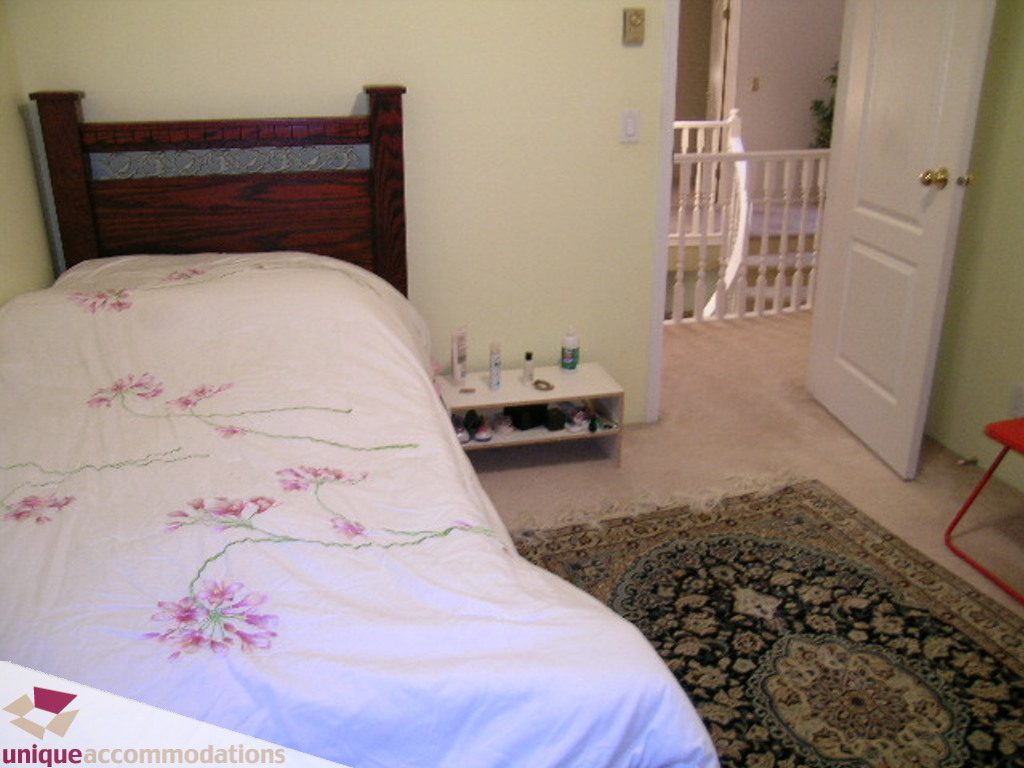 Furnished bedroom with floral bedding and a wooden headboard, adjacent to a baby gate. - 5735 Nancy Green way, North Vancouver