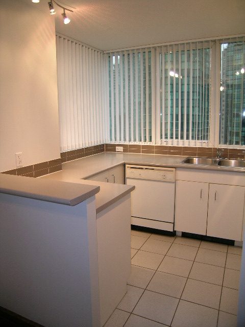 Bright kitchen with white cabinets, gray countertops, and city view through vertical blinds. - 2006 - 588 Broughton St, Vancouver Downtown