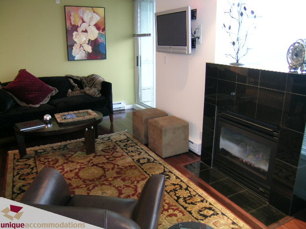 Furnished living room with a fireplace, patterned rug, and wall-mounted TV. - 2907 - 1328 W Pender St, Vancouver Downtown