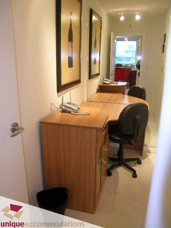 Furnished office with wooden desk, black chair, and framed wine bottle art. - 2907 - 1328 W Pender St, Vancouver Downtown