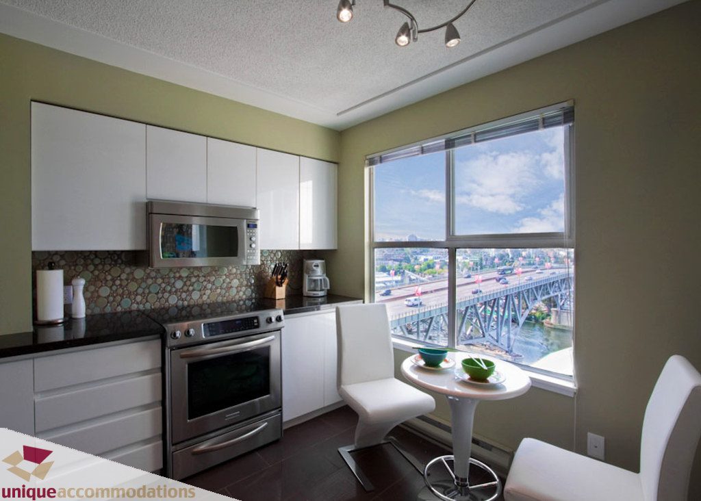Bright kitchen with stainless steel appliances, black countertops, and a city view. - 1806 - 1500 Howe St, Vancouver Downtown