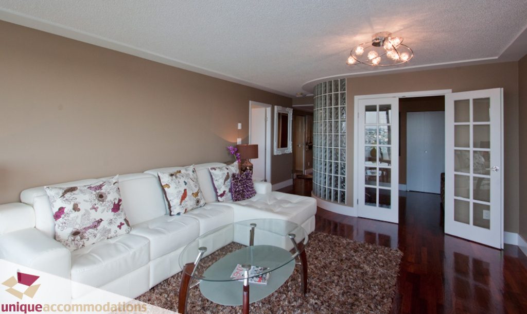 Furnished living room with white leather couch, glass coffee table, hardwood floors, and a wine storage column.