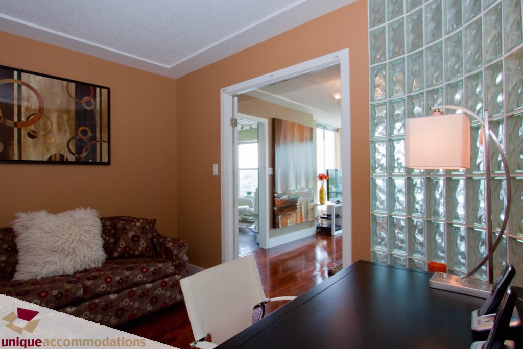 Furnished living room with hardwood floors, glass block wall, and modern decor. - 1806 - 1500 Howe St, Vancouver Downtown