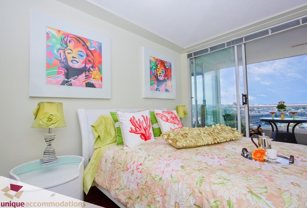 Bright bedroom with floral bedding, city view, and colorful artwork. - 1806 - 1500 Howe St, Vancouver Downtown