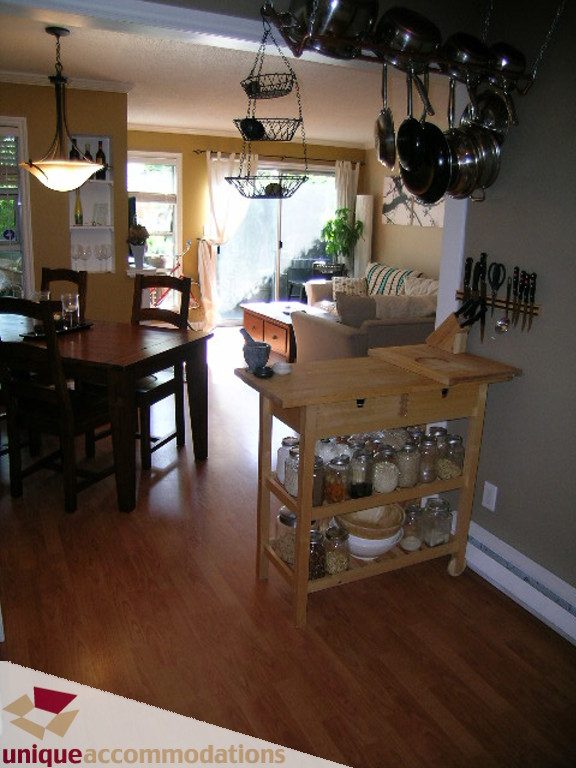 Bright kitchen with wooden island, hardwood floors, and hanging pots, leading to a cozy living area. - 50 - 900 West 17th, North Vancouver